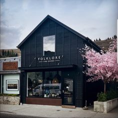 the store front of tolklore is black and has pink trees in blooming