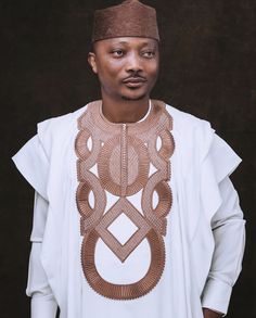 an african man wearing a white shirt and brown headdress, standing in front of a black background