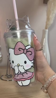 a person holding up a hello kitty cup with a straw in her hand, on a table