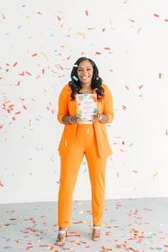 a woman in an orange jumpsuit holding up a book surrounded by confetti