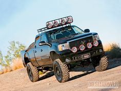 a black truck with four lights on it's flatbed driving down a dirt road