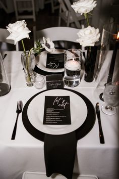 the table is set with black and white place settings, silverware, and flowers