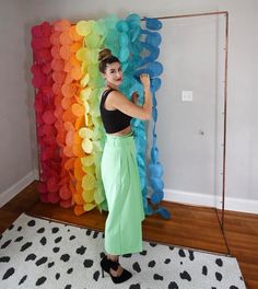 a woman standing in front of a rainbow backdrop with balloons on it and her arms up