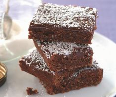 three pieces of chocolate brownies on a white plate with powdered sugar around them