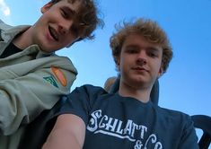 two young men sitting next to each other in front of a blue cloud filled sky