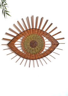 an eye made out of bamboo sticks is hanging on the wall next to a plant