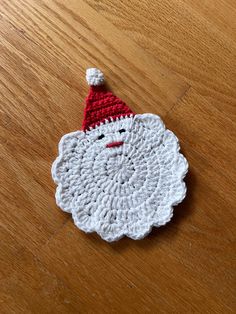 a crocheted santa clause ornament sitting on a wooden table with a red and white hat