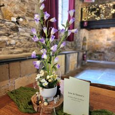 purple flowers are in a white pot on a wooden table next to a notepad