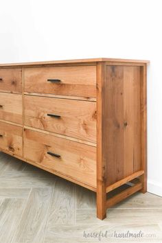 a wooden dresser sitting on top of a hard wood floor next to a white wall