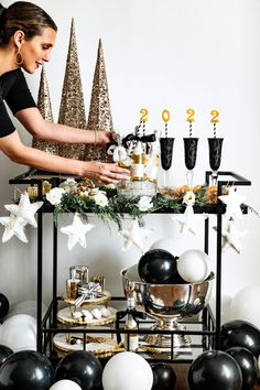 a woman is decorating a table with black and white balloons, silver and gold christmas decorations