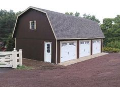 a brown barn with two garage doors and a white fence