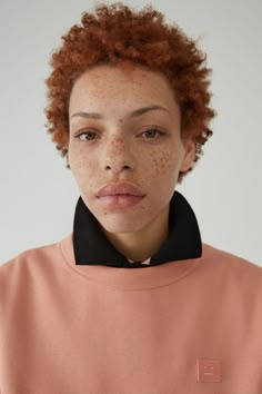 a woman with freckles on her face wearing a pink sweater and black collar