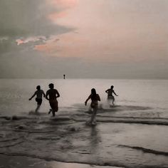 four people running into the ocean at sunset