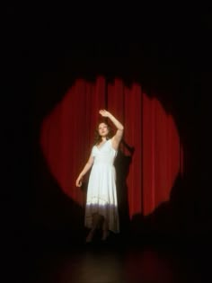 a woman standing in front of a red curtain with her hand up to the side