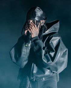 a man with dreadlocks is holding his hands to his face while standing in front of a dark background