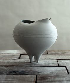 a small white vase sitting on top of a wooden table next to a wall and floor