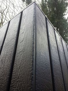 the top of a wooden structure with rain drops on it and trees in the background