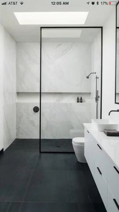 a white bathroom with black tile flooring and skylights above the shower area is shown