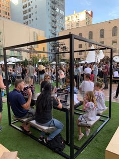 many people are sitting on the grass in front of an open box with a laptop