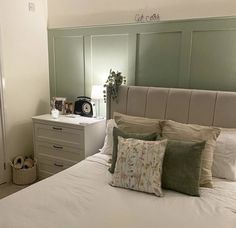 a white bed topped with lots of pillows next to a night stand and dressers