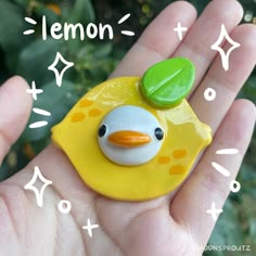 a hand holding a yellow toy with a green leaf on it's head and the words lemon above it