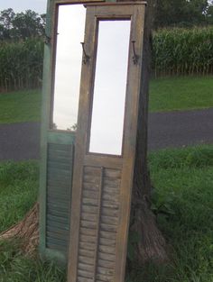 an old wooden door sitting in the grass next to a tree with a mirror on it