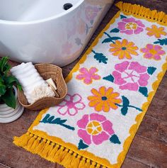 a bathroom rug with flowers on it next to a bathtub and potted plant