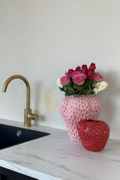 two vases with roses in them sitting on a counter top next to a faucet