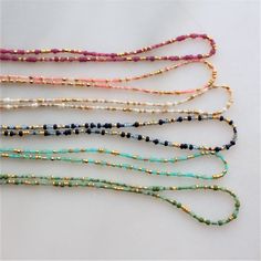 five different colored beaded necklaces on a white surface