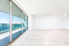 an empty room with large glass doors and white walls, overlooking the ocean from it's balcony