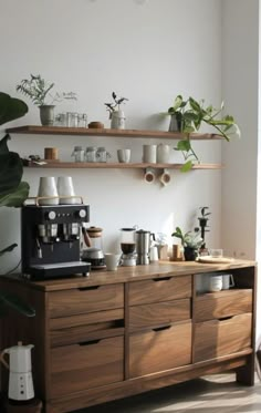 a coffee maker on top of a wooden cabinet in a room with plants and other items