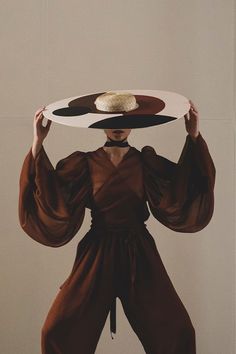 a woman holding a plate with two plates on it's head and wearing a brown outfit