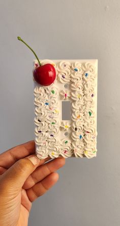 someone is holding up a decorative light switch plate with a cherry on it