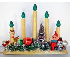 a candle holder with candles and christmas decorations on it, including a small elf sitting in the center