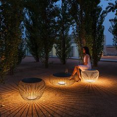 a woman sitting on a bench in the middle of some trees with lights shining through it