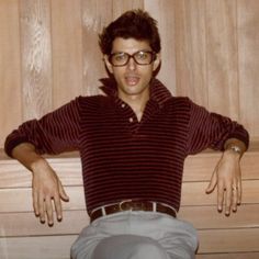 a man sitting on a bench with his hands behind his back and legs crossed, in front of wood paneling