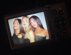 three women are on the screen of a cell phone in the dark, and one is wearing a black strapless top