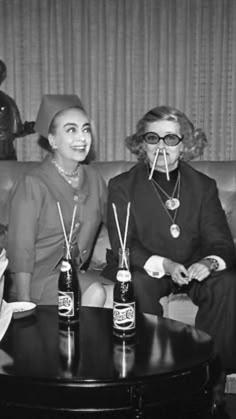 two women sitting on a couch with beer bottles in front of them and one woman wearing glasses