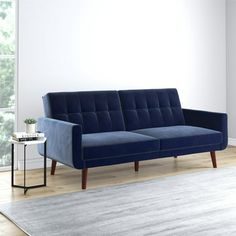 a blue couch sitting on top of a wooden floor next to a white rug and window