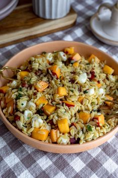 a bowl filled with rice and vegetables on top of a checkered table cloth next to a cup