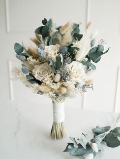 a bridal bouquet with white flowers and greenery on a marble countertop in front of a white wall