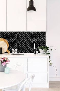 a white kitchen with black and white tile backsplashing on the back wall