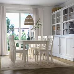 a white dining room table and chairs in front of a large window with open curtains