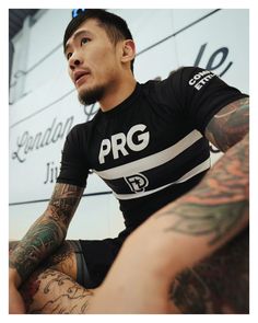 a man with tattoos sitting on the ground next to a sign that says pgg