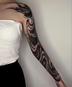 a woman's arm with black and grey swirls on it, in front of a white wall