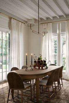 a dining room table surrounded by chairs with candles on it and windows in the background