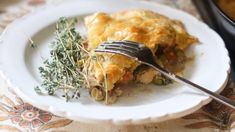 a white plate topped with an omelet covered in cheese and herbs next to a fork