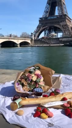 a table with bread, fruit and wine on it in front of the eiffel tower