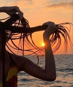 a woman standing on the beach with her hair blowing in the wind and sun setting behind her