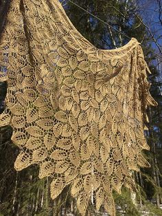 a crocheted shawl hanging from a wire in front of some pine trees